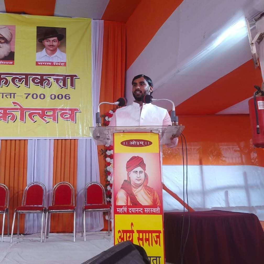 Pandit Umesh Arya addressing an Arya Samaj Kolkata utsav, with a portrait of Maharshi Dayanand Saraswati on the podium